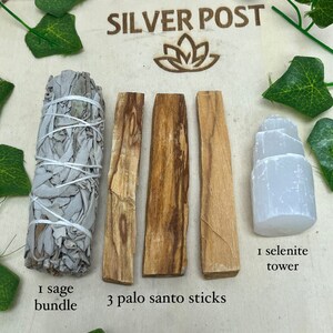 May include: A wooden board with three brown palo santo sticks, a white sage bundle, and a white selenite tower. The text "SILVER POST" is printed on the board. The text "1 sage bundle", "3 palo santo sticks", and "1 selenite tower" is printed below the items.