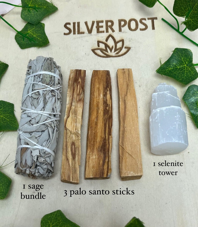 May include: A wooden board with three brown palo santo sticks, a white sage bundle, and a white selenite tower. The text "SILVER POST" is printed on the board. The text "1 sage bundle", "3 palo santo sticks", and "1 selenite tower" is printed below the items.
