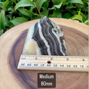 May include: A medium-sized, banded onyx crystal, approximately 8 cm tall, with a natural, polished finish. The stone features layers of black, white, and cream colors. The text "Medium 80mm" is visible.