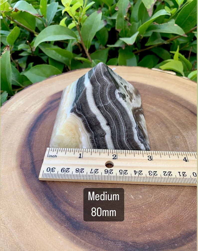 May include: A medium-sized, banded onyx crystal, approximately 8 cm tall, with a natural, polished finish. The stone features layers of black, white, and cream colors. The text "Medium 80mm" is visible.