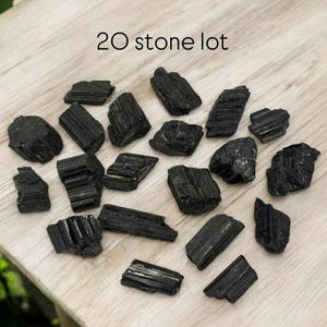 May include: A lot of 20 black tourmaline stones on a wooden surface. The stones are rough and have a natural, unpolished look.