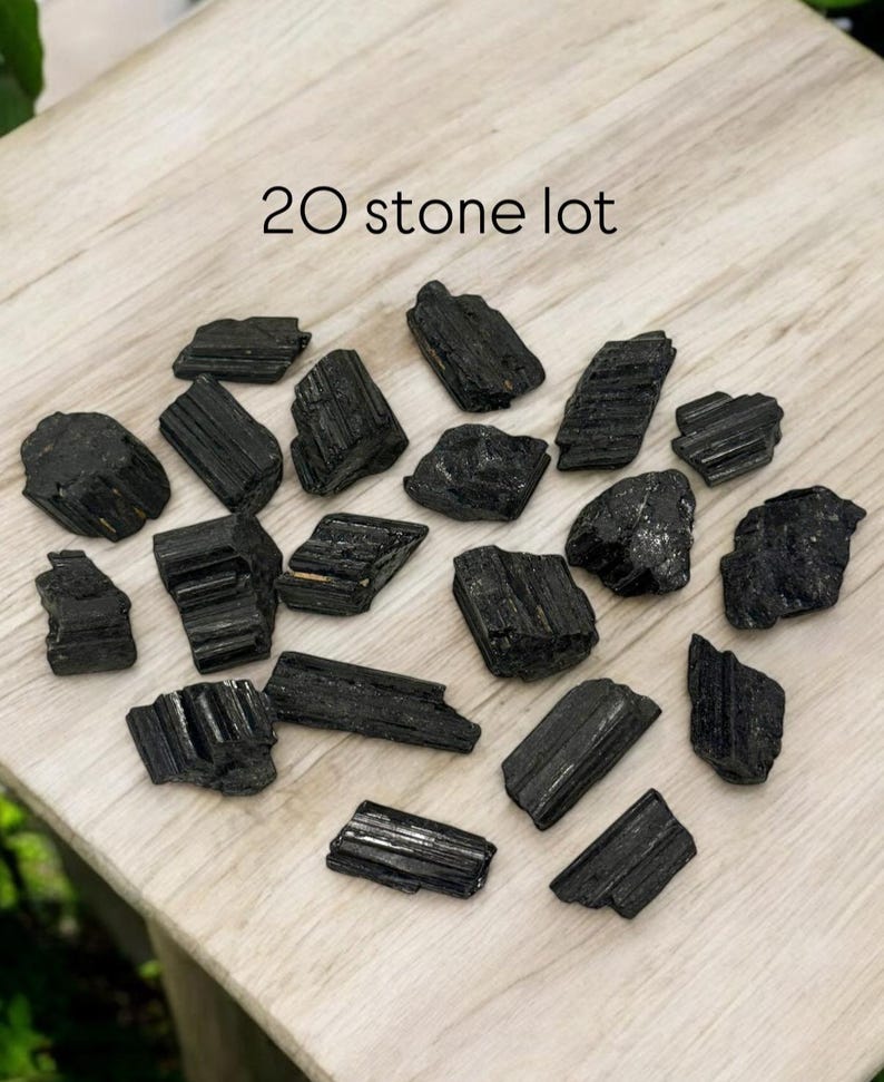 May include: A lot of 20 black tourmaline stones on a wooden surface. The stones are rough and have a natural, unpolished look.