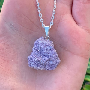 Op de afbeelding: Een zilveren ketting met een ruwe, paarse lepidolietkristal hanger. De kristal is ruw en heeft een natuurlijke, onregelmatige vorm.