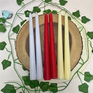 May include: Four taper candles on a wooden base. The candles are white, red, and cream.
