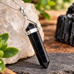 May include: A black tourmaline crystal pendant shaped into a polished hexagonal point. The stone is encased in a silver-toned metal cap with a triangular bail, suspended from a delicate silver-toned box chain necklace with a smooth, reflective finish.