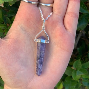 May include: A silver chain necklace with a purple crystal pendant. The pendant is a long, pointed crystal with a silver setting.