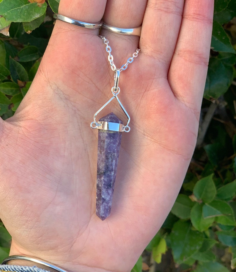 May include: A silver chain necklace with a purple crystal pendant. The pendant is a long, pointed crystal with a silver setting.