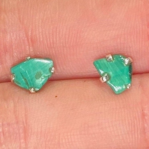 May include: A pair of silver earrings with green malachite stones. The stones are irregular in shape and have a natural, raw look.