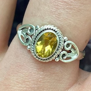 May include: A silver ring with an oval-shaped yellow gemstone set in a decorative filigree design.