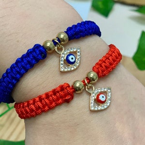 May include: Two adjustable bracelets with evil eye charms. One bracelet is red and the other is blue. Both charms have gold settings and rhinestones.