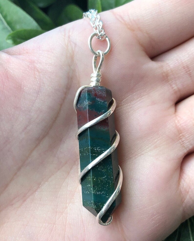 May include: A silver wire-wrapped pendant featuring a green, red, and brown jasper stone. The stone is a long, rectangular shape and is wrapped in silver wire in a spiral pattern.