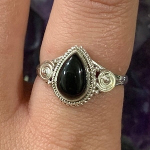 May include: A silver ring with a black teardrop-shaped gemstone set in a decorative silver setting.