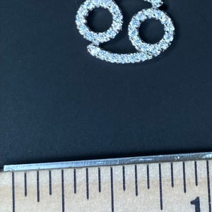 May include: A silver pendant necklace with a clear crystal Cancer zodiac sign charm. The pendant is about 1 inch in size.