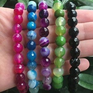 May include: Six bracelets made of faceted gemstone beads. The bracelets are in the colors pink, blue, purple, green, and black.