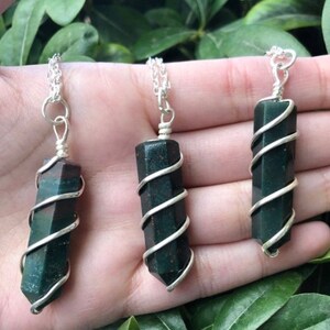 May include: Three silver necklaces with green and black gemstone pendants wrapped in silver wire. The pendants are all different shapes and sizes.