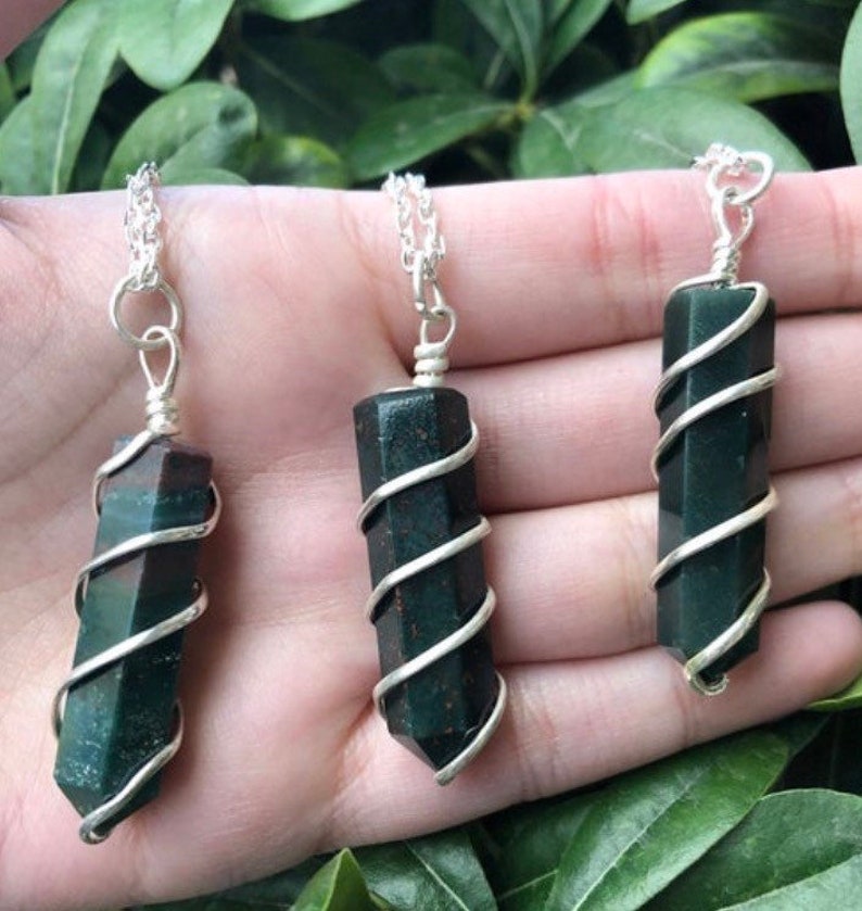 May include: Three silver necklaces with green and black gemstone pendants wrapped in silver wire. The pendants are all different shapes and sizes.
