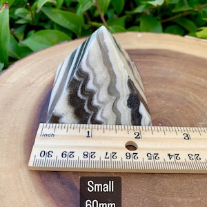 May include: A small, pyramid-shaped stone with a layered pattern of black, tan, and cream colours. The stone is approximately 5 cm in height. The text "Small 60mm" is visible.