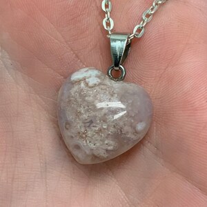 Puede incluir: Un collar de cadena de plata con un colgante en forma de coraz&oacute;n hecho de &aacute;gata blanca y rosa claro. La &aacute;gata tiene un patr&oacute;n de remolino de blanco y rosa claro.