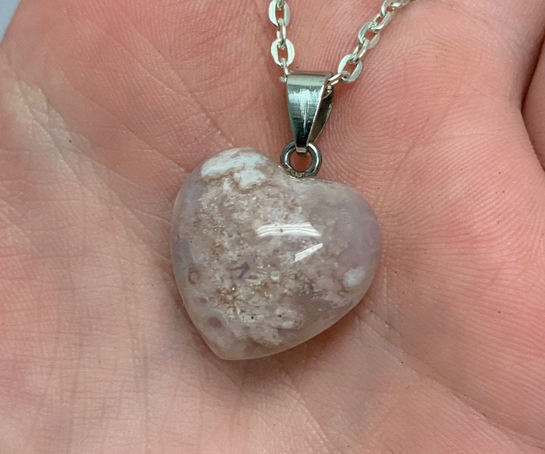Puede incluir: Un collar de cadena de plata con un colgante en forma de coraz&oacute;n hecho de &aacute;gata blanca y rosa claro. La &aacute;gata tiene un patr&oacute;n de remolino de blanco y rosa claro.