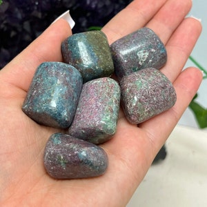 May include: A collection of six tumbled green and pink stones. The stones are smooth and have a mottled appearance.