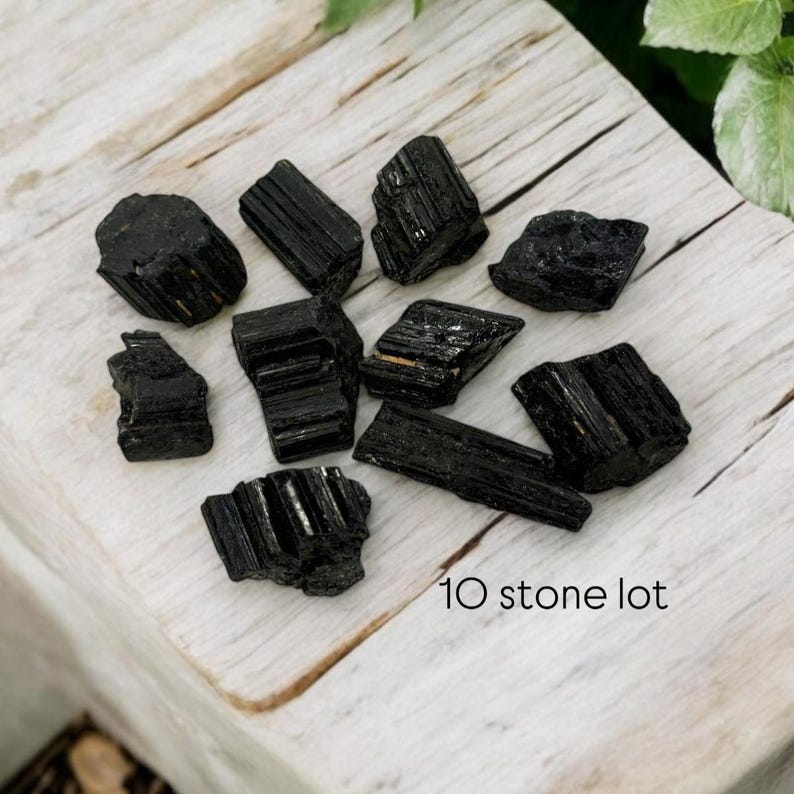 May include: A lot of ten black tourmaline stones, also known as schorl, on a white wooden surface.  The stones are rough and have a natural, unpolished finish.  10 stone lot.