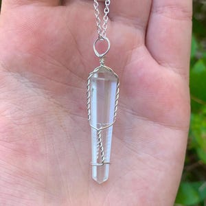 May include: A clear quartz crystal pendant wrapped in silver wire, hanging from a silver chain.