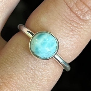 May include: A silver ring with a round, light blue gemstone. The gemstone has a marbled pattern.