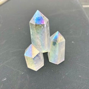K&ouml;nnte beinhalten: Drei regenbogenfarbene, klare Quarzkristallspitzen. Die Kristalle sind in Dreiecksform angeordnet. Die Kristalle sind glatt und haben einen leichten Regenbogen-Schimmer.