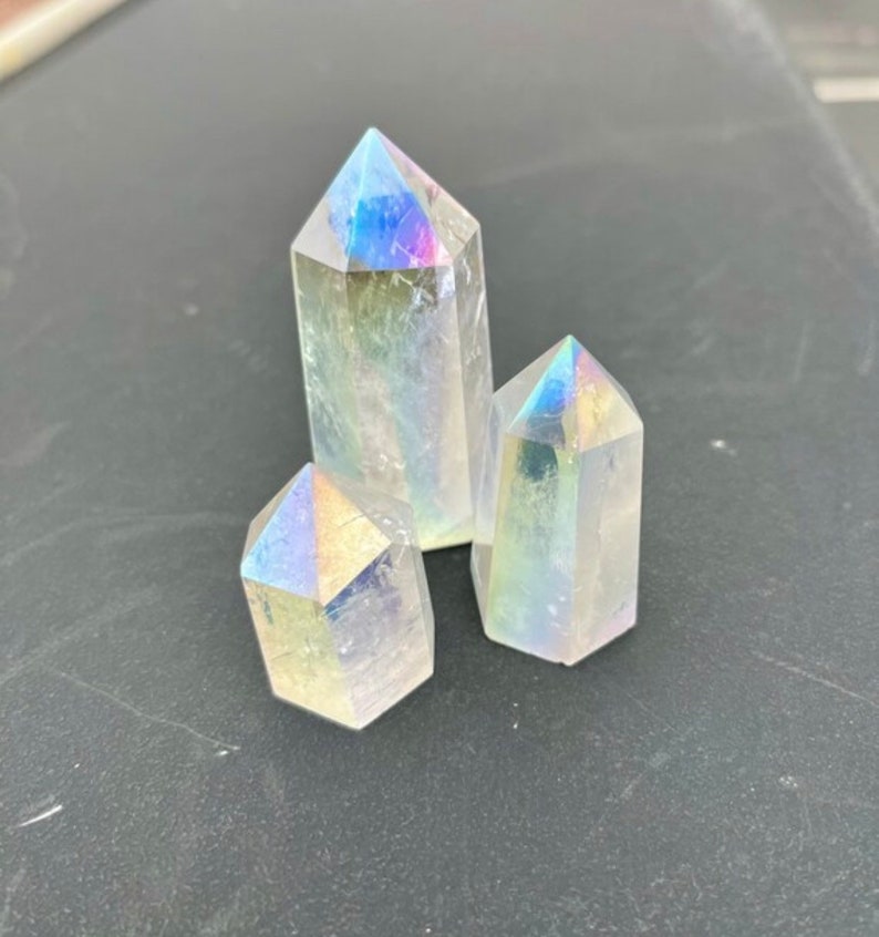K&ouml;nnte beinhalten: Drei regenbogenfarbene, klare Quarzkristallspitzen. Die Kristalle sind in Dreiecksform angeordnet. Die Kristalle sind glatt und haben einen leichten Regenbogen-Schimmer.