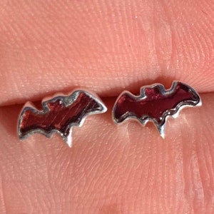 May include: A pair of silver stud earrings shaped like bats with red enamel filling.