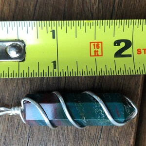 May include: A green, red, and brown stone pendant wrapped in silver wire on a silver chain. The pendant is approximately 2 inches long.