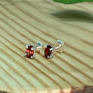 May include: A pair of silver stud earrings with oval-shaped red gemstones.
