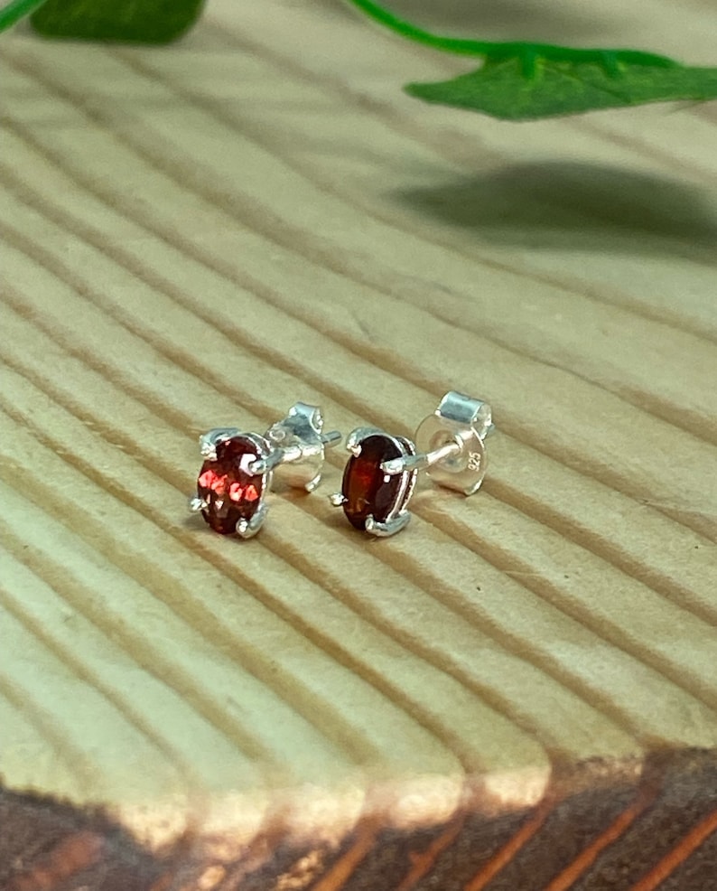 May include: A pair of silver stud earrings with oval-shaped red gemstones.