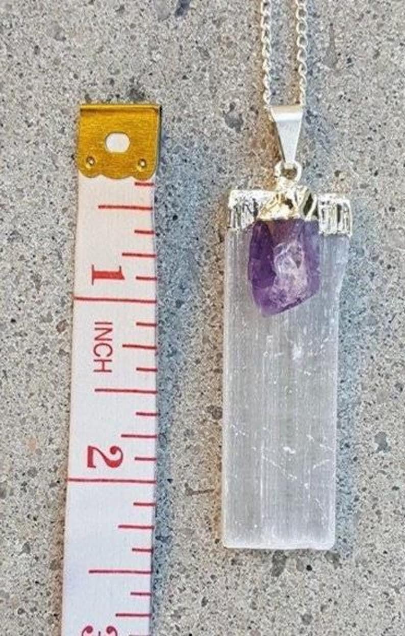 May include: A silver chain necklace with a white selenite crystal pendant and a small amethyst crystal. The pendant is approximately 1 inch in length.