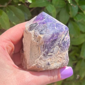 May include: A large, raw amethyst crystal with a natural point. The crystal is a deep purple color and has a rough, textured surface.
