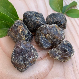 May include: Six dark brown amber stones of various sizes and shapes on a light brown wooden surface.