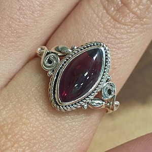 May include: A silver ring featuring a dark purple gemstone set in an intricate, ornate design.