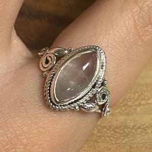 May include: A silver ring with a large, clear, faceted, oval-shaped gemstone. The ring has a detailed, ornate design.