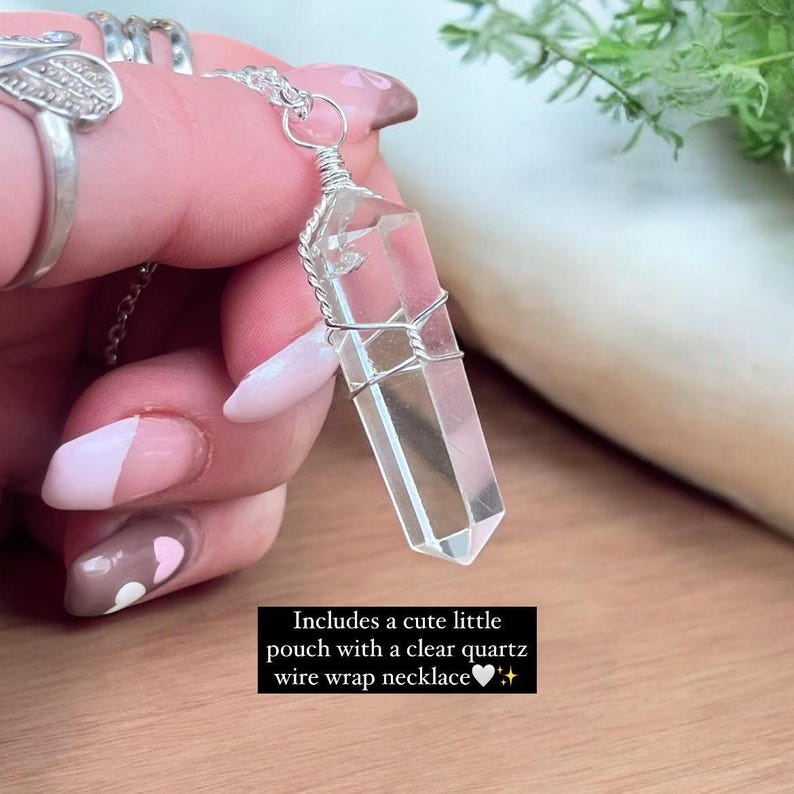 Puede incluir: Un colgante de cristal de cuarzo transparente envuelto en alambre plateado en una cadena de plata. El collar lo sostiene una mano con un dise&ntilde;o de u&ntilde;as en forma de coraz&oacute;n. El texto "Incluye una linda bolsita con un collar de alambre envuelto en cuarzo transparente" est&aacute; debajo de la imagen.