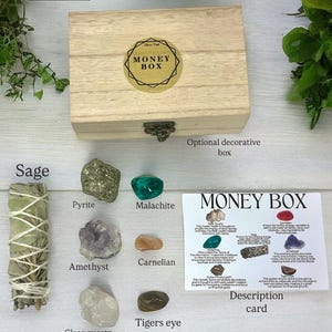 Peut inclure: Une bo&icirc;te en bois avec une &eacute;tiquette dor&eacute;e indiquant "Money Box". La bo&icirc;te est entour&eacute;e de divers cristaux et d'un b&acirc;tonnet de sauge. Les cristaux comprennent l'am&eacute;thyste, le quartz clair, la cornaline, la malachite, la pyrite et l'&oelig;il de tigre. Une carte avec le titre "Money Box" et des descriptions des cristaux est &eacute;galement incluse.
