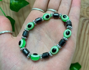 Könnte beinhalten: Ein grünes und schwarzes böses Auge Armband mit silbernen Perlen. Das Armband besteht aus mehreren Perlen, darunter runde grüne und schwarze böse Auge Perlen und silberne Abstandshalter Perlen.