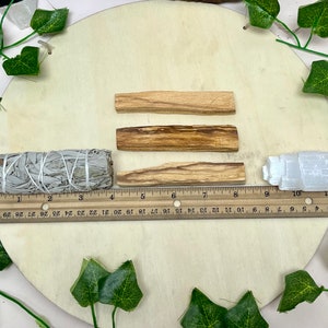 May include: Three brown wooden sticks, a white sage smudge stick, and a white selenite crystal on a wooden surface. The sticks are approximately 4 inches long. The sage stick is approximately 4 inches long. The selenite crystal is approximately 2 inches tall.