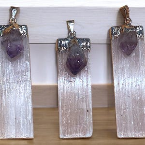 May include: Three silver and gold pendants with a white selenite crystal and a purple amethyst point. The pendants are rectangular and have a smooth, polished finish.