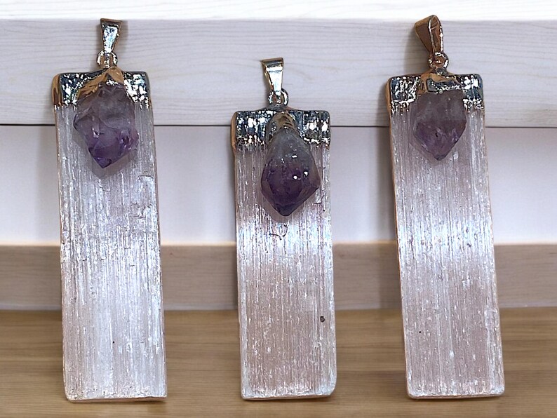 May include: Three silver and gold pendants with a white selenite crystal and a purple amethyst point. The pendants are rectangular and have a smooth, polished finish.