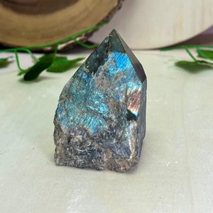 May include: A blue and green labradorite crystal point with iridescent shimmer. The crystal is rough and natural, with a pointed top and a flat base.