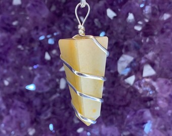 May include: A yellow crystal pendulum wrapped in silver wire, hanging from a silver chain. The pendulum is a pointed shape and is set against a background of purple amethyst crystals.