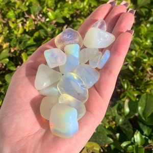 May include: A collection of iridescent white opal tumbled stones. The stones are smooth and polished, with a variety of shapes and sizes.