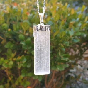 May include: A silver chain necklace with a white selenite crystal pendant. The pendant is a rectangular shape with a silver bezel setting.