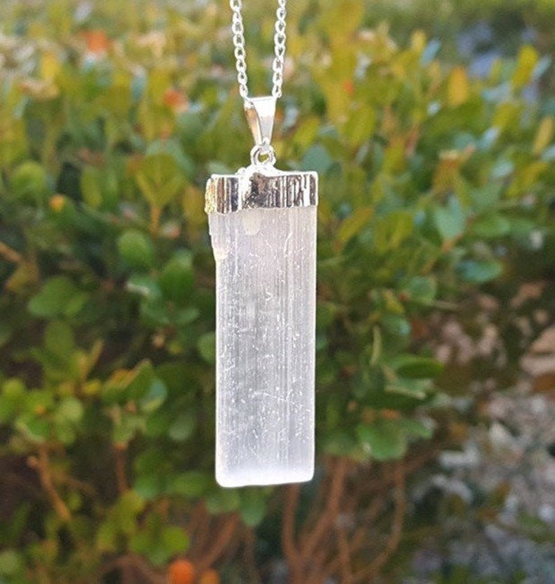 May include: A silver chain necklace with a white selenite crystal pendant. The pendant is a rectangular shape with a silver bezel setting.