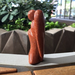 May include: A small, red-brown, carved stone angel figurine with a glittery finish.